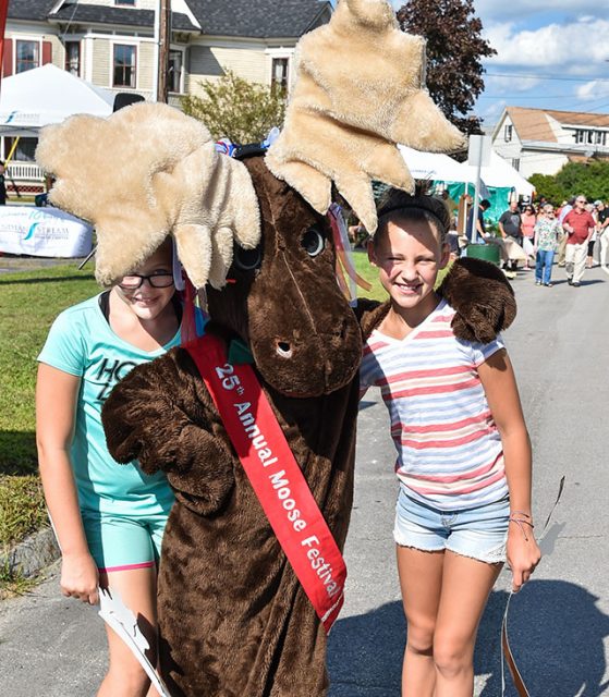 Two children with person in moose costume posing for photo